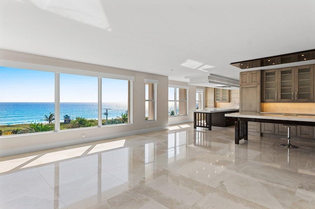 kitchen with marble finish floor, light countertops, a water view, glass insert cabinets, and baseboards