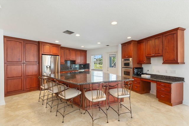 kitchen with built in desk, stainless steel appliances, dark stone counters, and a kitchen island