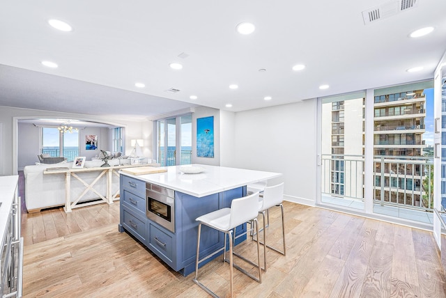 kitchen featuring stainless steel microwave, a kitchen bar, light hardwood / wood-style floors, and a kitchen island