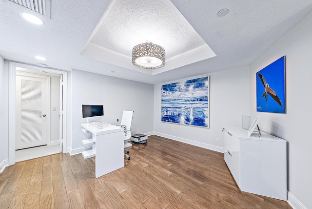 home office with hardwood / wood-style floors, a raised ceiling, and a textured ceiling