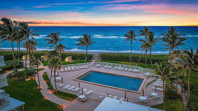 pool at dusk with a water view and a patio area