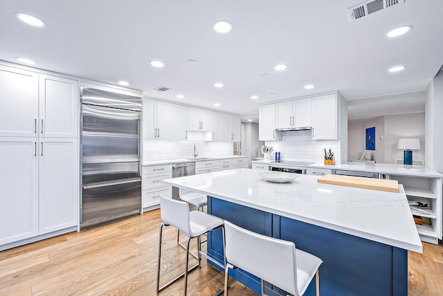 kitchen with a breakfast bar, white cabinets, light stone counters, stainless steel appliances, and light hardwood / wood-style flooring