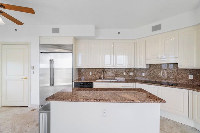 kitchen featuring a kitchen island, stainless steel built in refrigerator, sink, dark stone countertops, and black electric stovetop