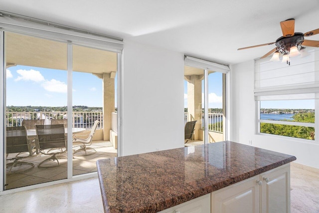 kitchen with white cabinets, dark stone counters, ceiling fan, floor to ceiling windows, and a water view