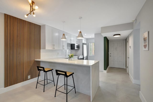 kitchen featuring decorative light fixtures, appliances with stainless steel finishes, kitchen peninsula, decorative backsplash, and white cabinets