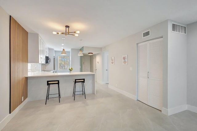 kitchen featuring a breakfast bar area, white cabinetry, tasteful backsplash, kitchen peninsula, and pendant lighting