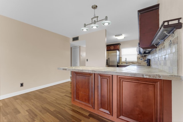 kitchen featuring hardwood / wood-style floors, decorative backsplash, hanging light fixtures, range, and stainless steel refrigerator with ice dispenser