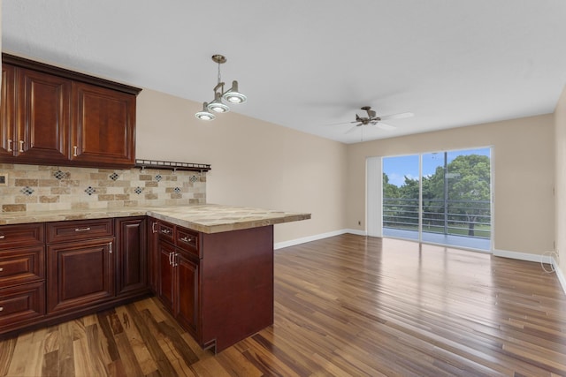 kitchen with ceiling fan with notable chandelier, pendant lighting, backsplash, dark hardwood / wood-style flooring, and kitchen peninsula