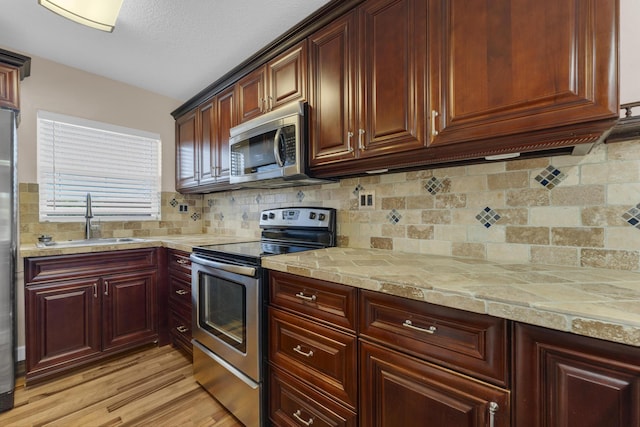 kitchen featuring sink, backsplash, stainless steel appliances, light stone countertops, and light wood-type flooring