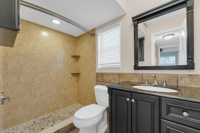 bathroom with tiled shower, vanity, toilet, and tile walls