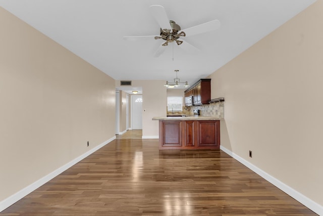 interior space with dark wood-type flooring, tasteful backsplash, kitchen peninsula, pendant lighting, and ceiling fan with notable chandelier