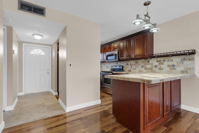 kitchen featuring pendant lighting, backsplash, stainless steel appliances, light hardwood / wood-style floors, and kitchen peninsula