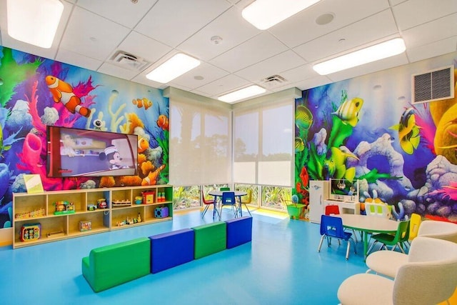 recreation room with floor to ceiling windows and a drop ceiling