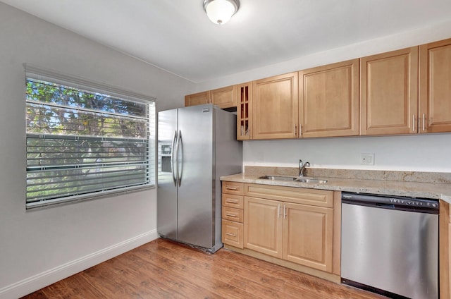 kitchen with sink, light stone counters, stainless steel appliances, light brown cabinets, and light hardwood / wood-style flooring