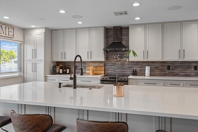 kitchen featuring sink, wall chimney range hood, a breakfast bar, and stainless steel electric range