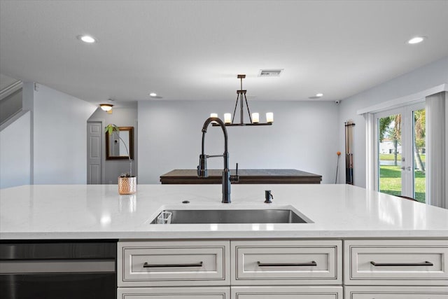 kitchen featuring sink, white cabinetry, light stone counters, a center island with sink, and pendant lighting