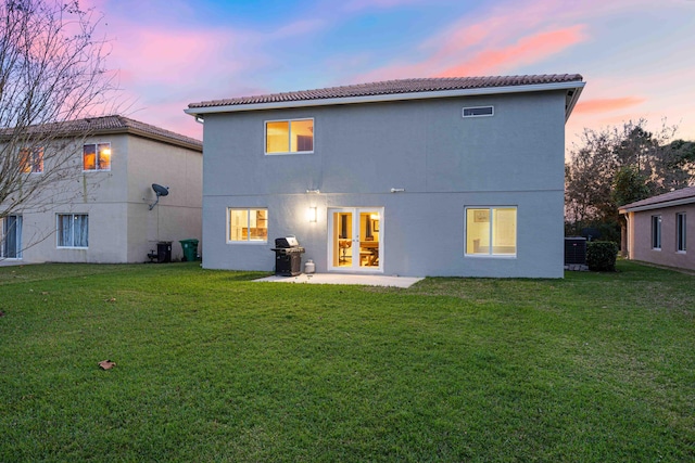 back house at dusk featuring cooling unit and a lawn