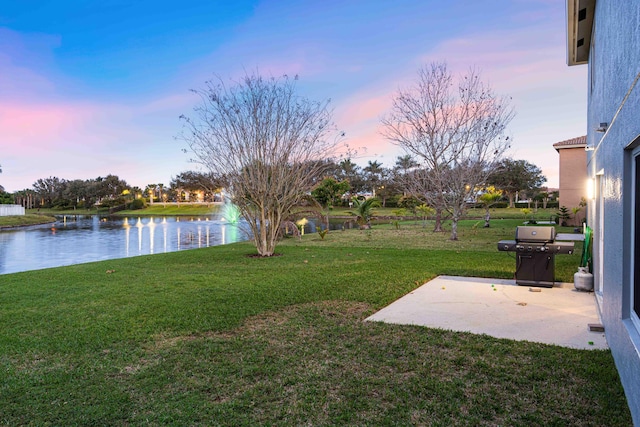 yard at dusk featuring a water view and a patio area