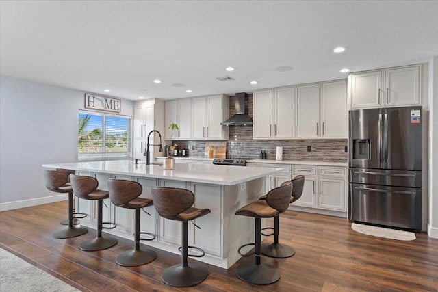 kitchen featuring a breakfast bar, stainless steel appliances, a center island with sink, decorative backsplash, and wall chimney exhaust hood