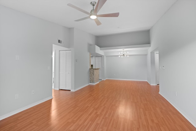 unfurnished living room with vaulted ceiling, ceiling fan with notable chandelier, and light hardwood / wood-style flooring