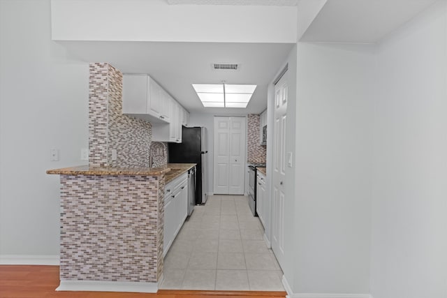 kitchen featuring light tile patterned floors, stone counters, appliances with stainless steel finishes, white cabinets, and decorative backsplash