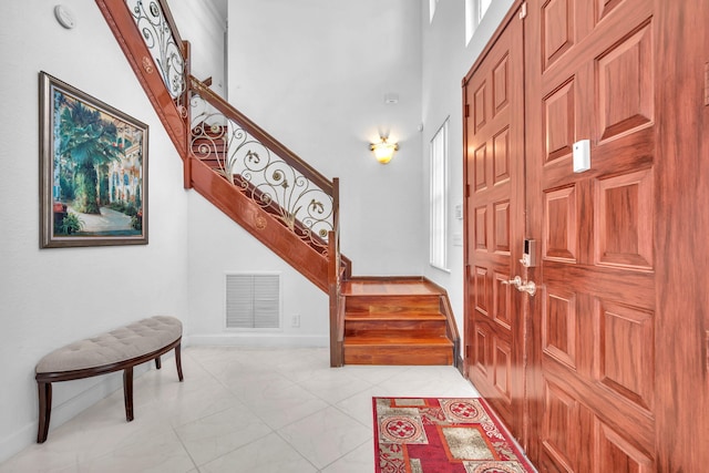 foyer entrance with visible vents, a towering ceiling, baseboards, and stairs