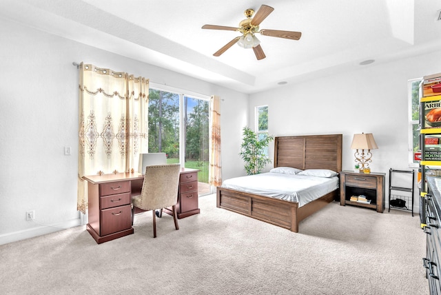 bedroom with light carpet, baseboards, a tray ceiling, and a ceiling fan