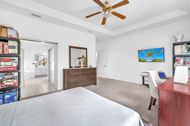 bedroom featuring light tile patterned floors, a raised ceiling, visible vents, light carpet, and ensuite bath