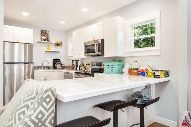 kitchen with a breakfast bar, stainless steel appliances, kitchen peninsula, and white cabinets