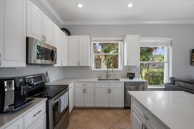 kitchen with light tile patterned flooring, appliances with stainless steel finishes, white cabinetry, sink, and ornamental molding