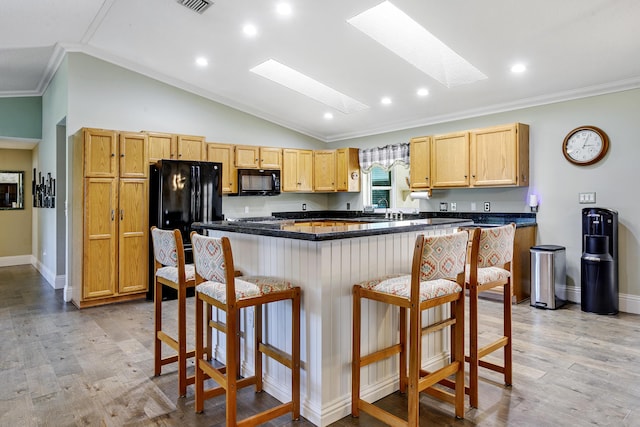 kitchen with light brown cabinetry, ornamental molding, black appliances, and a kitchen breakfast bar