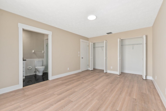 unfurnished bedroom featuring light wood-type flooring, two closets, and ensuite bath