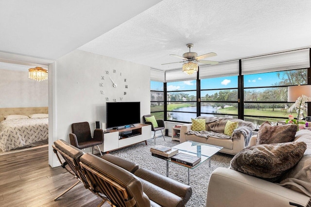 living room featuring ceiling fan with notable chandelier, hardwood / wood-style floors, and a textured ceiling