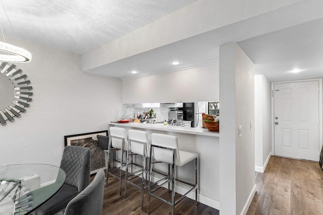 interior space featuring stainless steel refrigerator, tasteful backsplash, wood-type flooring, a kitchen bar, and kitchen peninsula