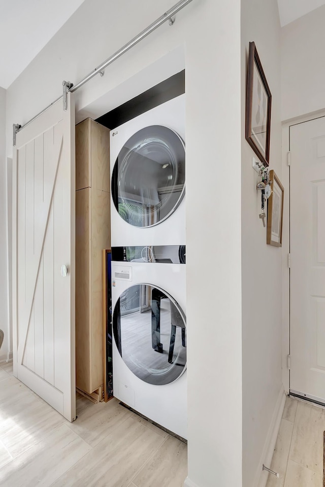 clothes washing area with stacked washer / dryer, a barn door, and light wood-type flooring