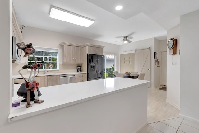 kitchen featuring stainless steel dishwasher, a barn door, kitchen peninsula, and black fridge