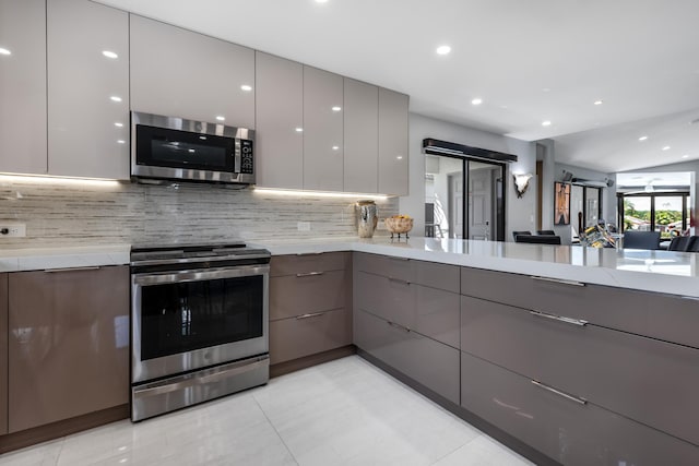 kitchen with gray cabinetry, backsplash, light stone countertops, and appliances with stainless steel finishes