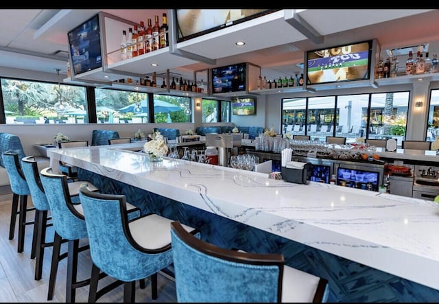 bar with wood-type flooring, a healthy amount of sunlight, and light stone counters