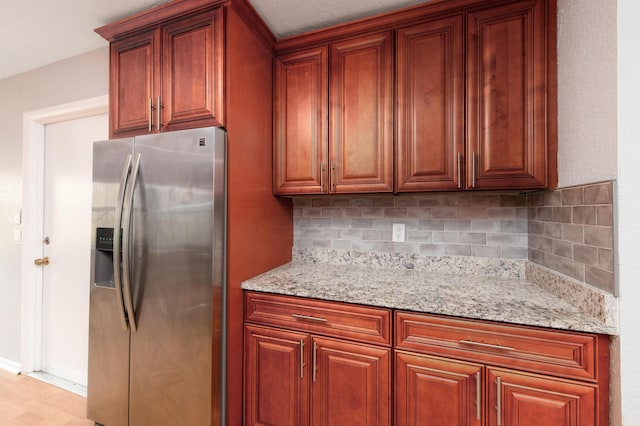 kitchen with tasteful backsplash, stainless steel fridge, light stone countertops, and light wood-type flooring