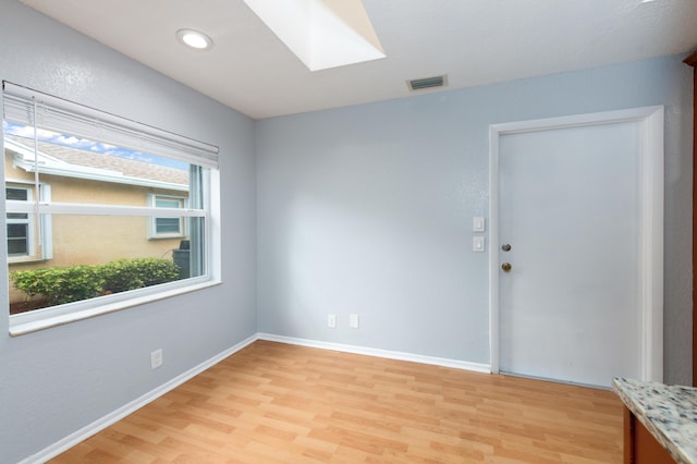 unfurnished room featuring a skylight and light hardwood / wood-style flooring