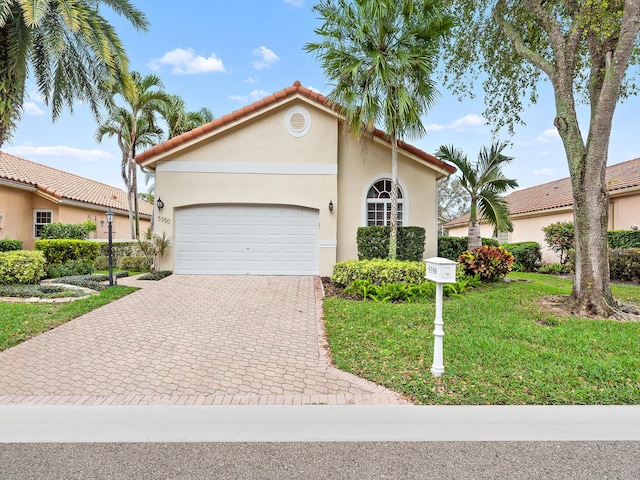 mediterranean / spanish-style home with a tile roof, an attached garage, decorative driveway, a front lawn, and stucco siding