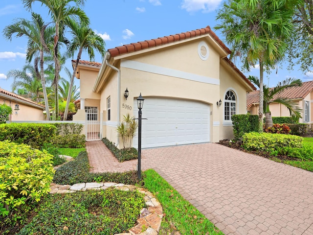 mediterranean / spanish-style home featuring a tile roof, an attached garage, fence, decorative driveway, and stucco siding