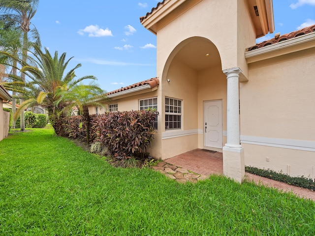 doorway to property with a tiled roof, a lawn, and stucco siding