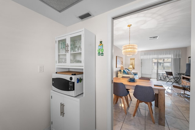 interior space featuring pendant lighting, a chandelier, light tile patterned floors, and white cabinets