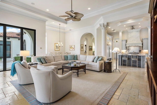 living room with ornamental molding, a tray ceiling, ceiling fan with notable chandelier, and a high ceiling