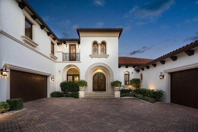 mediterranean / spanish house featuring a balcony, decorative driveway, stucco siding, and french doors