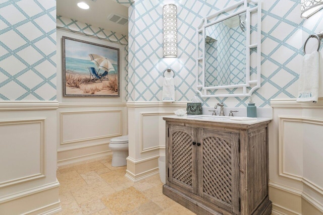 bathroom featuring a decorative wall, visible vents, toilet, and vanity