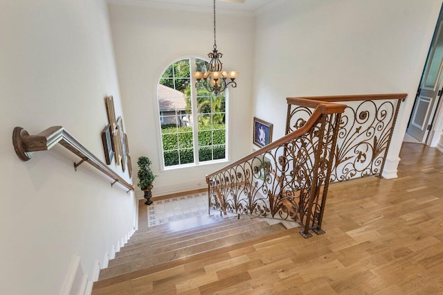 stairway with baseboards, ornamental molding, wood finished floors, and a notable chandelier
