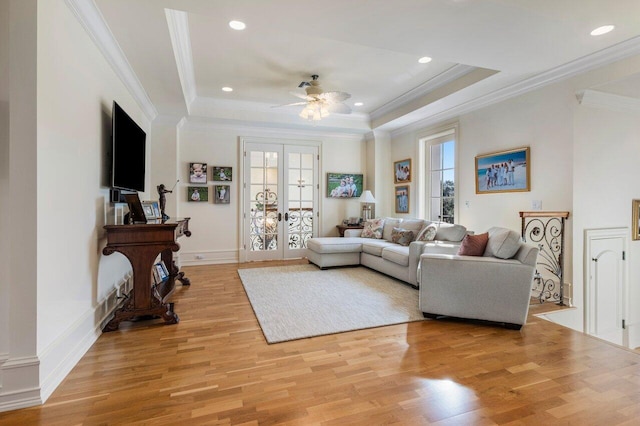 living area with a ceiling fan, light wood-style flooring, french doors, and a raised ceiling
