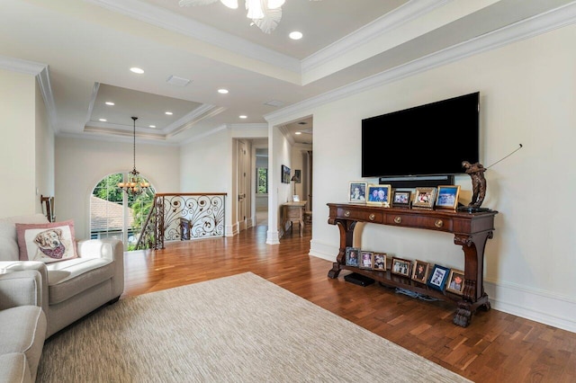 living room featuring a tray ceiling, crown molding, baseboards, a chandelier, and wood finished floors
